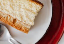 Closeup of red plate placed under white plate with appetizing piece of cake near tea spoon on table