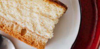 Closeup of red plate placed under white plate with appetizing piece of cake near tea spoon on table