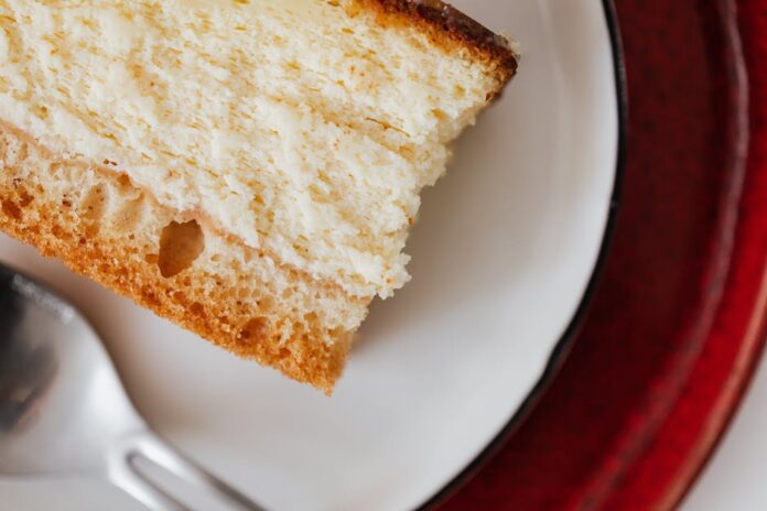 Closeup of red plate placed under white plate with appetizing piece of cake near tea spoon on table