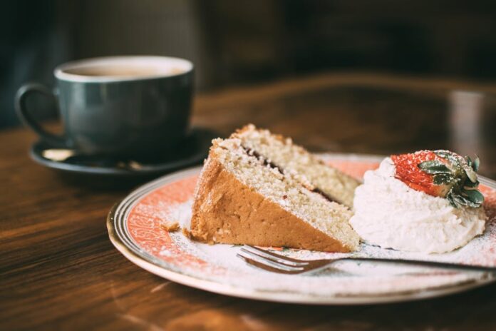 Bolo de morango com recheio de natas e gelatina: descubra! A slice of sponge cake with cream and strawberry, served with a hot cup of coffee, in a cozy café setting.