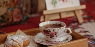 Vintage floral teacup with tea and pastries on a wooden tray creates a cozy home atmosphere.
