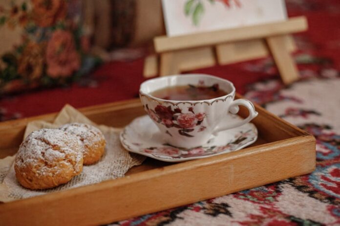 Vintage floral teacup with tea and pastries on a wooden tray creates a cozy home atmosphere.