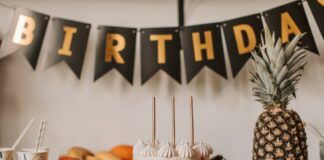 A colorful birthday cake with fruits and festive decorations on a table indoors.