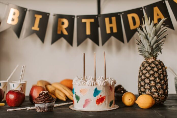 A colorful birthday cake with fruits and festive decorations on a table indoors.