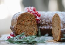 Appetizing homemade chocolate sponge cake with berries and rosemary sprig placed on table against blurred background