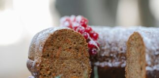 Appetizing homemade chocolate sponge cake with berries and rosemary sprig placed on table against blurred background