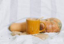 Warm autumn drink in a yellow mug with pumpkin and squash on a soft background.