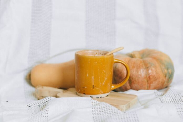 Warm autumn drink in a yellow mug with pumpkin and squash on a soft background.