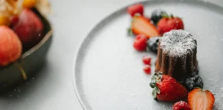 Bolo de chocolate branco com framboesas delicioso From above of palatable homemade pie sprinkled with icing sugar placed on round plate on table near blurred bowl in kitchen