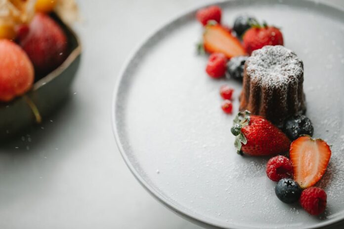 From above of palatable homemade pie sprinkled with icing sugar placed on round plate on table near blurred bowl in kitchen