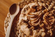 Top view of a freshly baked apple galette on a woven placemat with a wooden spoon beside it.