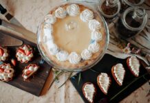 Top view of appetizing cake and desserts with whipped cream near knives and flowers on table