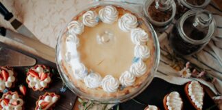 Top view of appetizing cake and desserts with whipped cream near knives and flowers on table