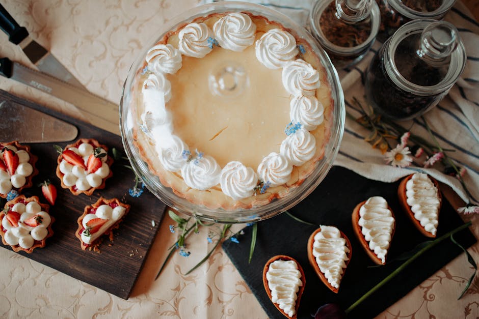 Top view of appetizing cake and desserts with whipped cream near knives and flowers on table
