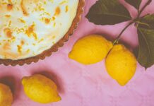 Receita de torta de limão com cobertura de merengue irresistível Elegant lemon meringue pie with zest accents and fresh lemons on a vibrant pink background.