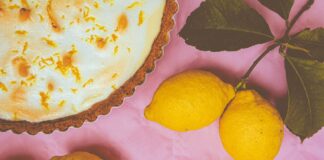 Elegant lemon meringue pie with zest accents and fresh lemons on a vibrant pink background.