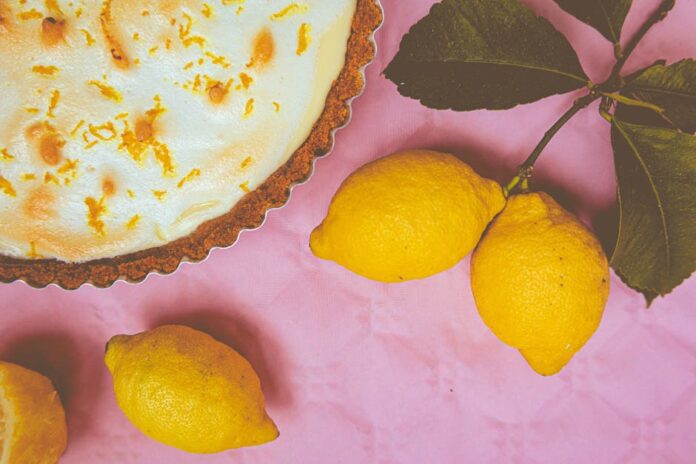 Receita de Torta de Limão com Cobertura de Merengue Irresistível Elegant lemon meringue pie with zest accents and fresh lemons on a vibrant pink background.