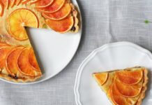 Receita fácil de bolo de laranja caseiro com calda irresistível Freshly baked orange citrus tart with a slice served on a white plate.