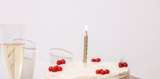 A white frosted cake adorned with red berries and a lit candle, perfect for celebrations.