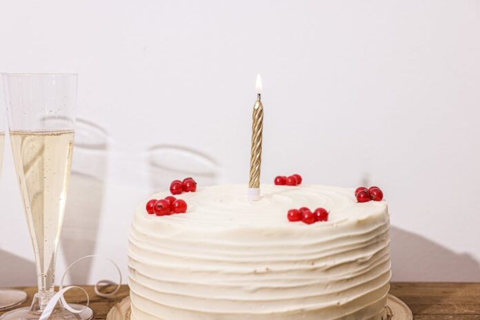 Receita de Bolo de Aniversário Simples e Bonito para Surpreender! A white frosted cake adorned with red berries and a lit candle, perfect for celebrations.