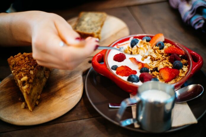 Receita de Bolo de Iogurte Rápido com Poucos Ingredientes Irresistível Close-up of a breakfast setting with granola, fresh berries, and a slice of cake.