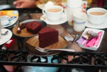 Bolo Fofo para lanche da tarde Red velvet cake slices with cups of coffee on a glass table, offering a cozy treat.