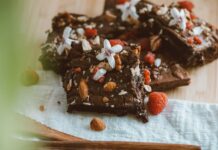 Close-up of chocolate brownies adorned with almonds, raspberries, and white flowers on a wooden board.