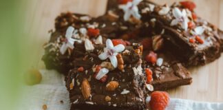Close-up of chocolate brownies adorned with almonds, raspberries, and white flowers on a wooden board.