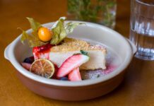 Receita de Cheesecake de Natal de Lima e Frutos Vermelhos irresistível Slice of cheesecake with fresh fruit and berry garnish in a ceramic dish.