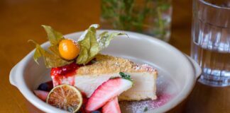 Slice of cheesecake with fresh fruit and berry garnish in a ceramic dish.
