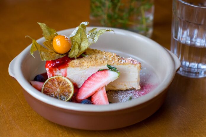 Receita de Cheesecake de Natal de Lima e Frutos Vermelhos Irresistível! Slice of cheesecake with fresh fruit and berry garnish in a ceramic dish.
