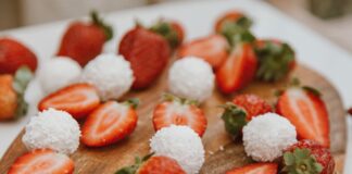 Appetizing strawberries and coconut balls arranged on a wooden board, perfect for dessert lovers.