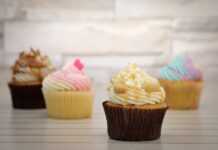 Bolinhos de amor: Descubra a receita que derrete corações Deliciously decorated cupcakes with colorful frosting displayed on a wooden surface, perfect for dessert lovers.