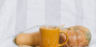 Warm autumn drink in a yellow mug with pumpkin and squash on a soft background.