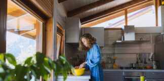 A woman with curly hair prepares a meal in a sunlit kitchen, surrounded by fresh fruits.