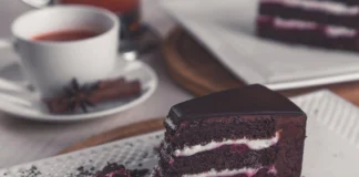 Bolo de Chocolate com flor de sal Closeup of a rich chocolate cake slice on a plate with a tea cup in the background.