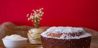 A mouthwatering homemade coconut cake with shredded coconut topping against a vibrant red backdrop.