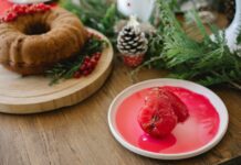 Bolo de Pera Rocha com Vinho do Porto: Uma delícia irresistível A holiday cake adorned with red berries and pinecones, accompanied by poached pears in syrup.