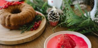 A holiday cake adorned with red berries and pinecones, accompanied by poached pears in syrup.