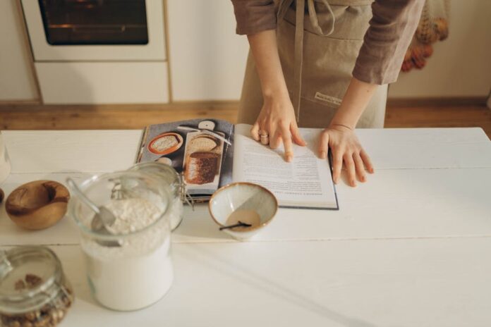 Bolo Rápido para Iniciantes: A Delícia que Você Precisa Tentar! Hands pointing at cookbook in a cozy kitchen setting with ingredients ready for baking.