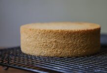 Receita de Bolo Caseiro simples e barato que surpreende A plain sponge cake cooling on a wire rack, ready for decoration or serving.