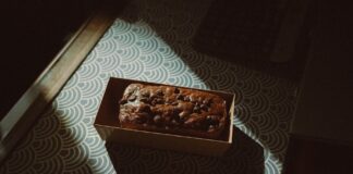 A delectable chocolate cake topped with chocolate chips in a box, captured in warm indoor lighting.