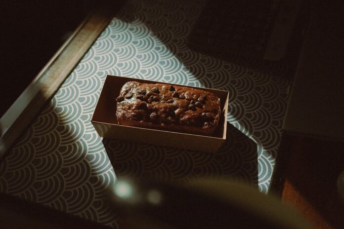 Receita de Bolo de Chocolate Simples para Iniciantes Incrível! A delectable chocolate cake topped with chocolate chips in a box, captured in warm indoor lighting.