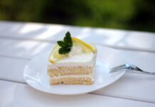 Receita de Bolo de Iogurte com limão: O Segredo da maciez Delicious lemon cream cake slice garnished with lemon and mint on white plate.