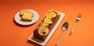 Bolo de Laranja caseiro rápido: Surpreenda-se Freshly baked citrus loaf cake topped with orange slices on a vibrant orange background.