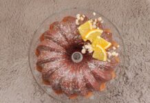Receita de Bolo de Laranja fofinho A delicious Bundt cake topped with orange slices and powdered sugar on a textured surface.