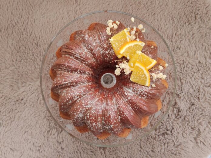 Receita de Bolo de Laranja Fofinho: O Lanche Perfeito! A delicious Bundt cake topped with orange slices and powdered sugar on a textured surface.