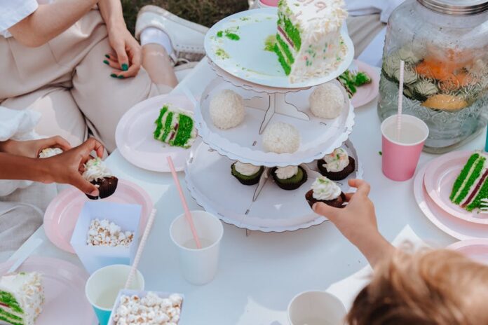 Receita de bolo para lanche das crianças que elas vão adorar! Adults and children enjoying a festive garden party with vibrant cakes and cupcakes.