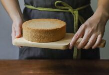 Receita de Bolo simples para o lanche da tarde irresistível A freshly baked sponge cake being held on a wooden board, ready to serve.