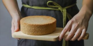 A freshly baked sponge cake being held on a wooden board, ready to serve.